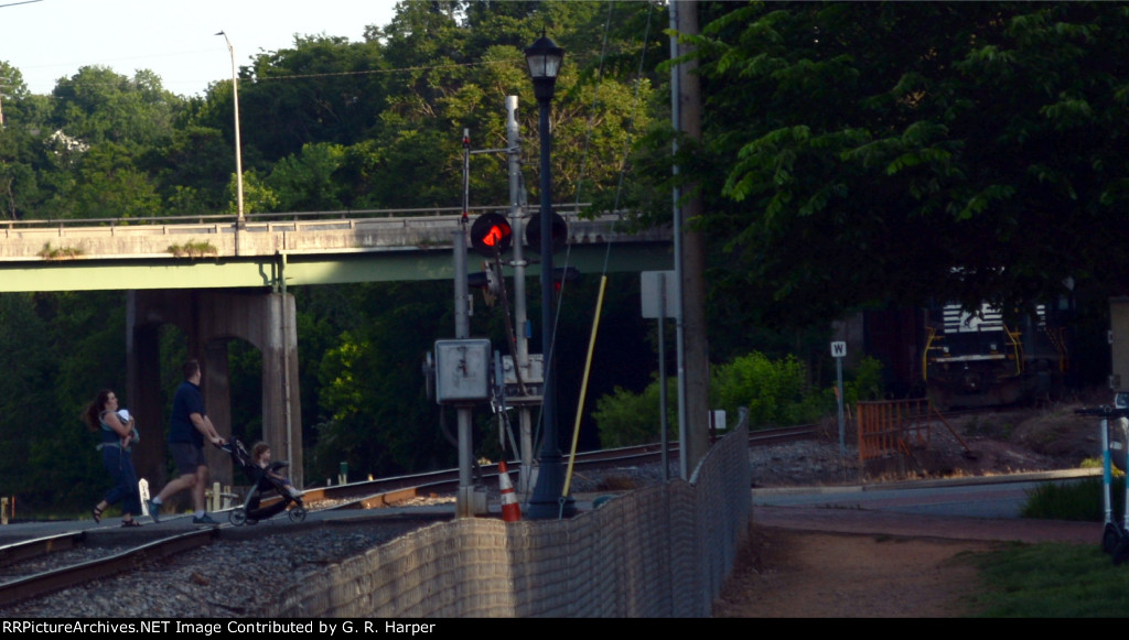 A family hustles across the Washington St. crossing as NS yard job E23 descends the Old Main Line hill with interchange traffic for CSX.